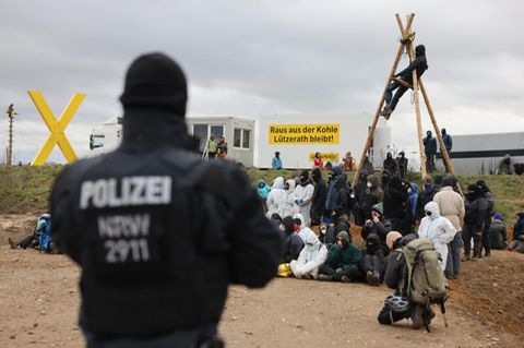 Ein Polizist beobachtet Klimaschutzaktivisten. die am Rand des Tagebaus sitzen