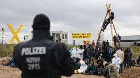 Ein Polizist beobachtet Klimaschutzaktivisten. die am Rand des Tagebaus sitzen