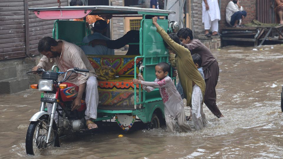 Menschen in Pakistan fahren eine Riksha durch eine überflutete Straße