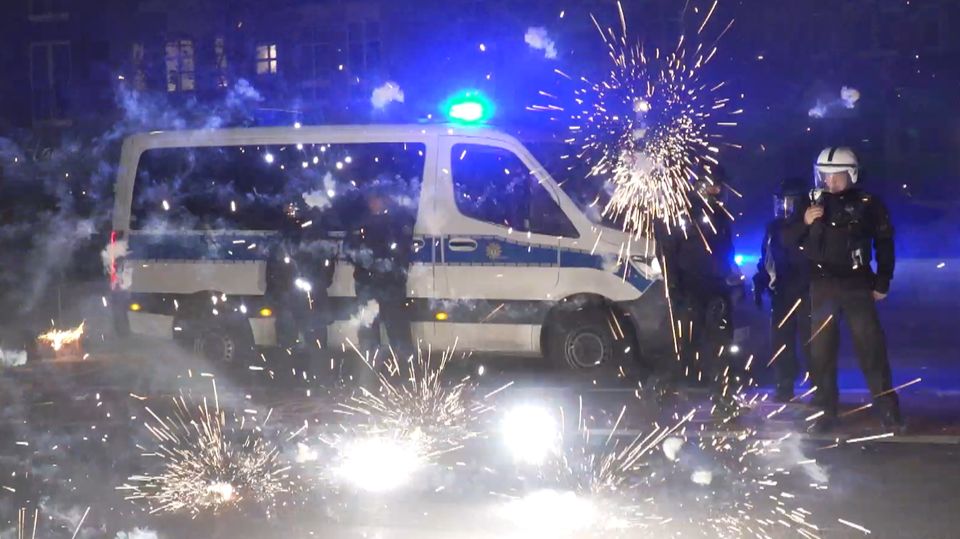 In Berlin stehen Polizisten in Schutzkleidung hinter explodierden Raketen neben ihrem Mannschaftswagen in Berlin