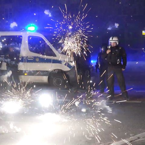 In Berlin stehen Polizisten in Schutzkleidung hinter explodierden Raketen neben ihrem Mannschaftswagen in Berlin