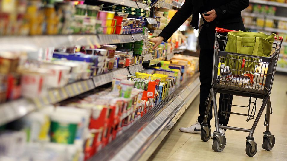 Ein Kunde mit Einkaufswagen neben einem Supermarktregal Inflation