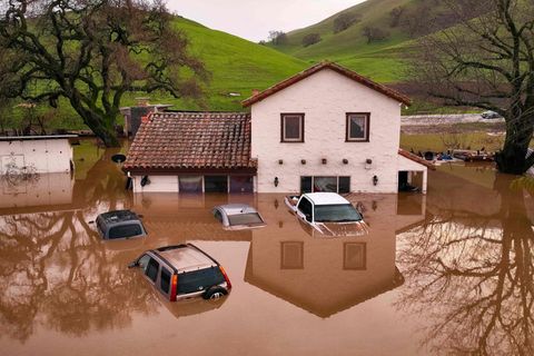 In Kalifornien ragen vor einem Haus vier Autos aus den Überschwemmungen