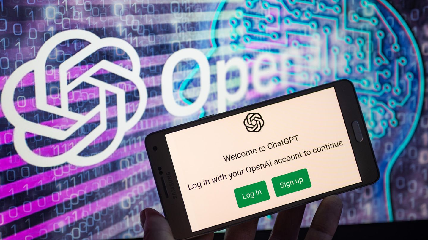Ein Smartphone mit dem geöffneten Chatbot ChatGPT, im Hintergrund das Logo "Open AI"