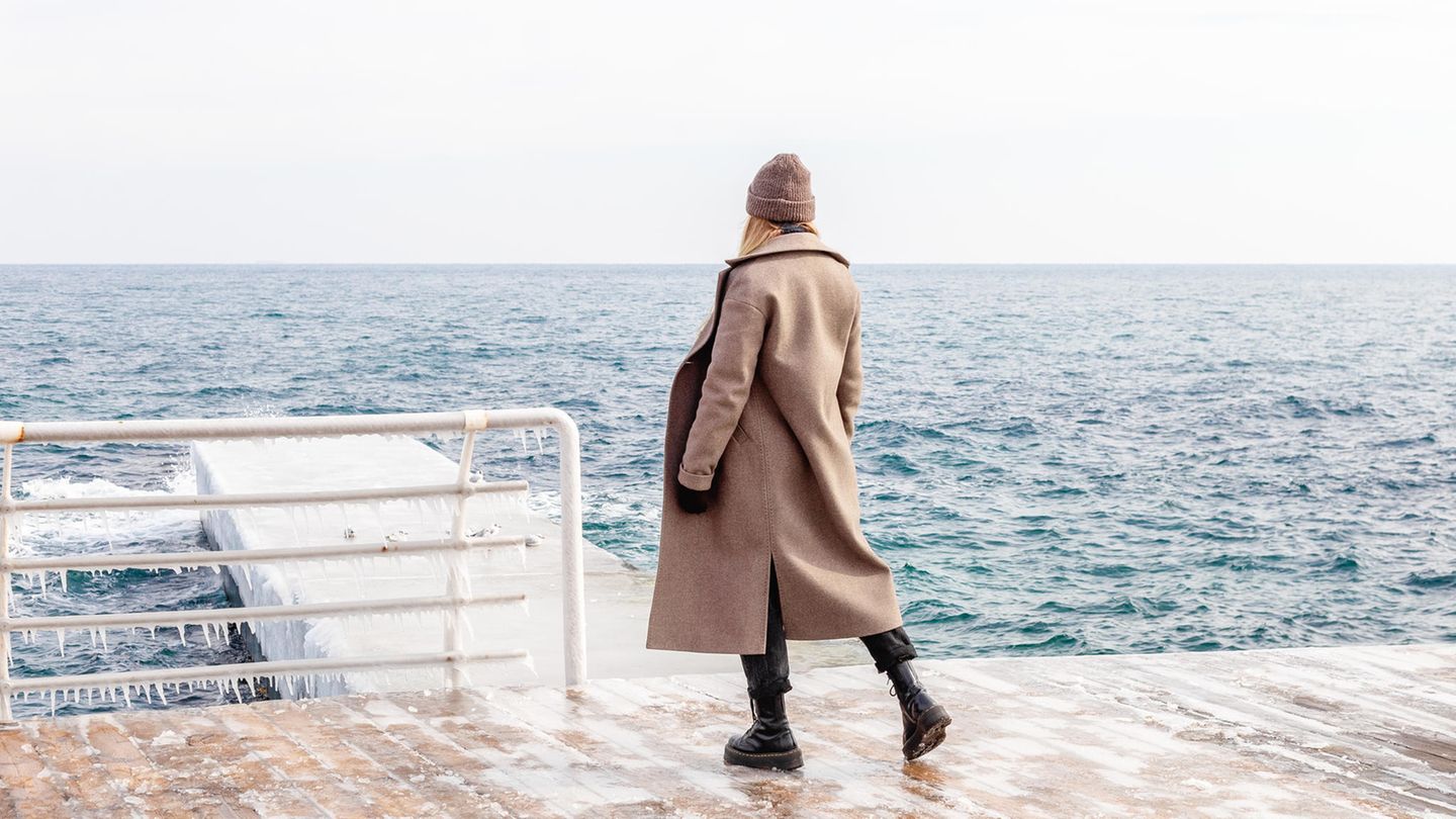 Coat trend 2023: Woman stands by the water and wears a wool coat