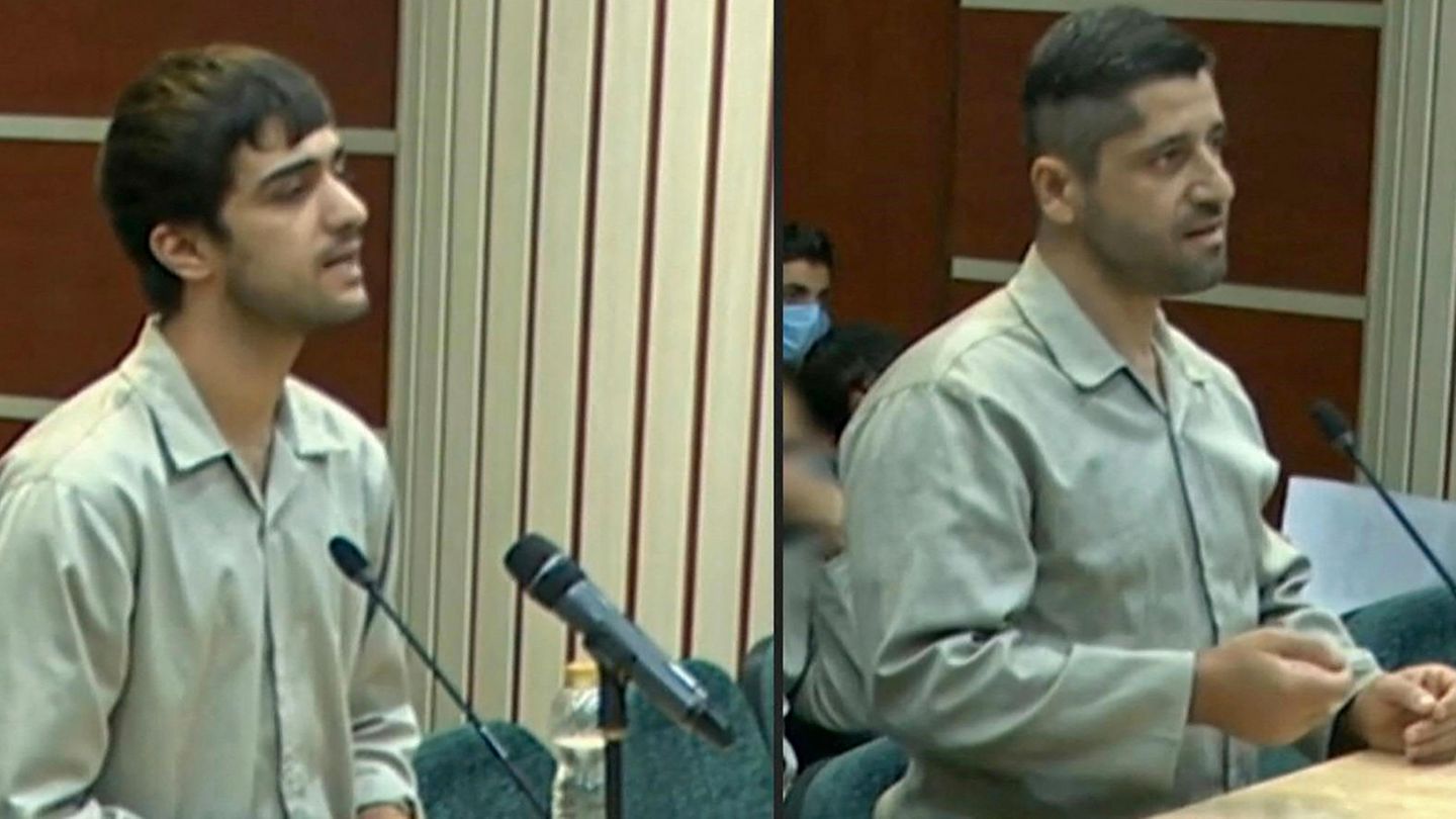 Im Iran sitzen zwei junge Männer in weißer Oberbekleidung in einem Gerichtssaal und sprechen in Mikrofone