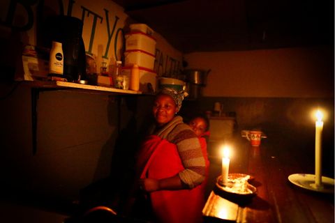  Eine Gastronomin aus Kapstadt muss ihr Imbissrestaurant bei Kerzenlicht betreiben. Es herrscht ein planmäßiger Stromausfalls, der als load shedding bekannt ist.