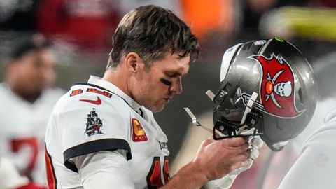 Tom Brady, ein weißer, blonder Football-Spieler geht mit gesenktem Kopf und einem weiß-roten Helm in beiden Händen