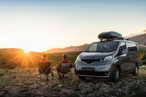 Zwei Menschen sitzen neben ihrem Camper auf Stühlen und gucken den Sonnenuntergang an