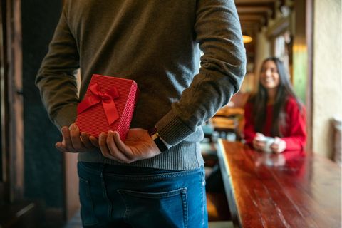 Valentinstag 2023: Mann mit Geschenk hinter dem Rücken in einem Restaurant
