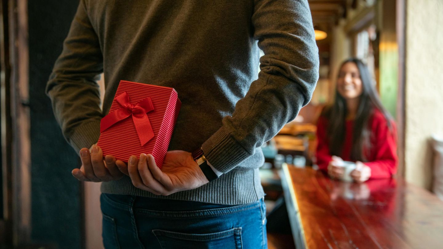 Valentinstag 2023: Mann mit Geschenk hinter dem Rücken in einem Restaurant