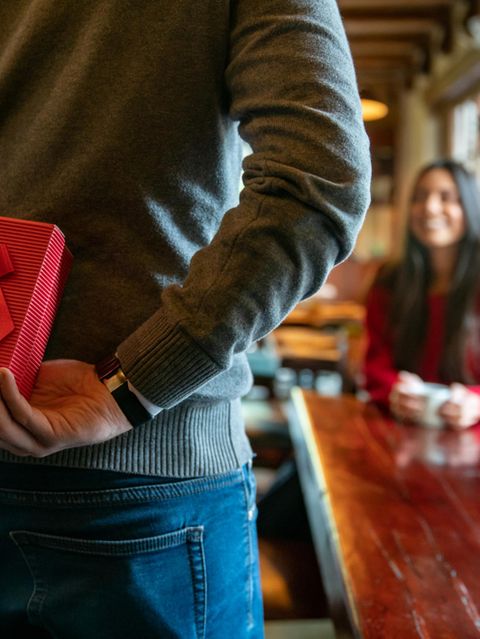 Valentinstag 2023: Mann mit Geschenk hinter dem Rücken in einem Restaurant