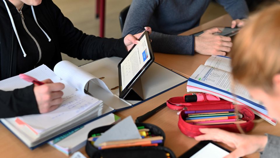 In einer Schulstunde sitzen drei Schülerinnen mit Tablets gemeinsam an einem Tisch