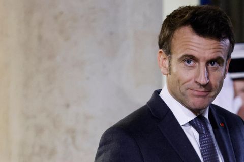 Emmanuel Macron, ein weißer Mann mit braunem Seitenscheitel, steht in dunkelblauem Anzug und weißem Hemd vor einer Säule
