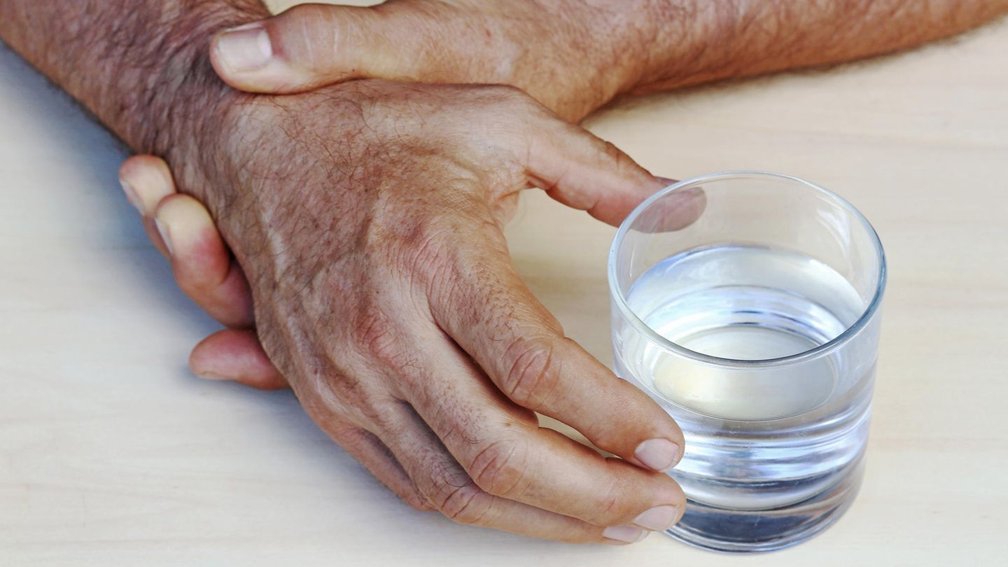 Zitternde Hände halten sich gegenseitig fest, um ein Glas zu greifen