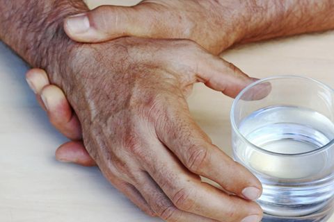 Zitternde Hände halten sich gegenseitig fest, um ein Glas zu greifen