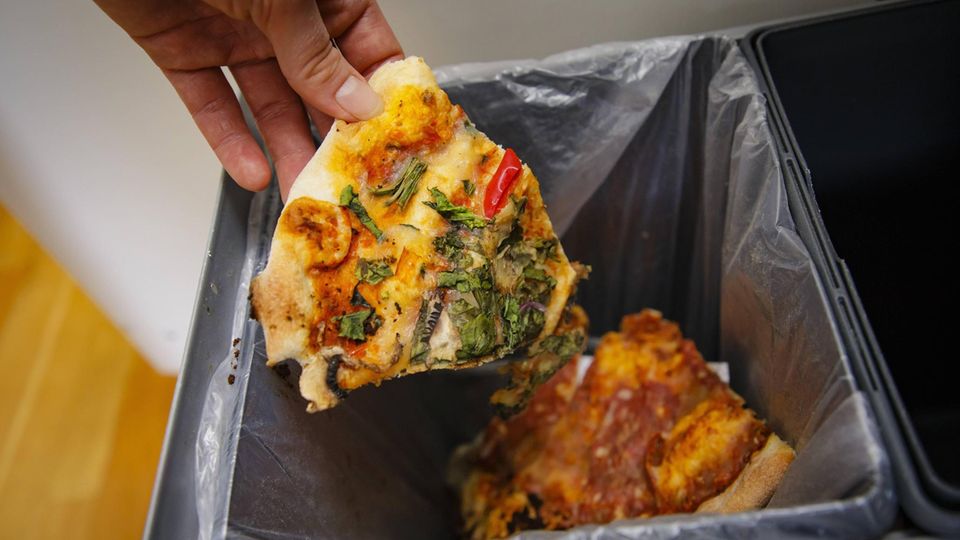 Eine Frau wirft ein Stück Pizza im Müll