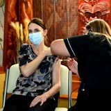 Jacinda Ardern sitzt auf einem Stuhl, während eine Frau in schwarzem Oberteil ihr eine Corona-Impfung in den Oberarm spritzt