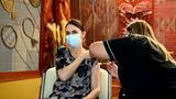 Jacinda Ardern sitzt auf einem Stuhl, während eine Frau in schwarzem Oberteil ihr eine Corona-Impfung in den Oberarm spritzt