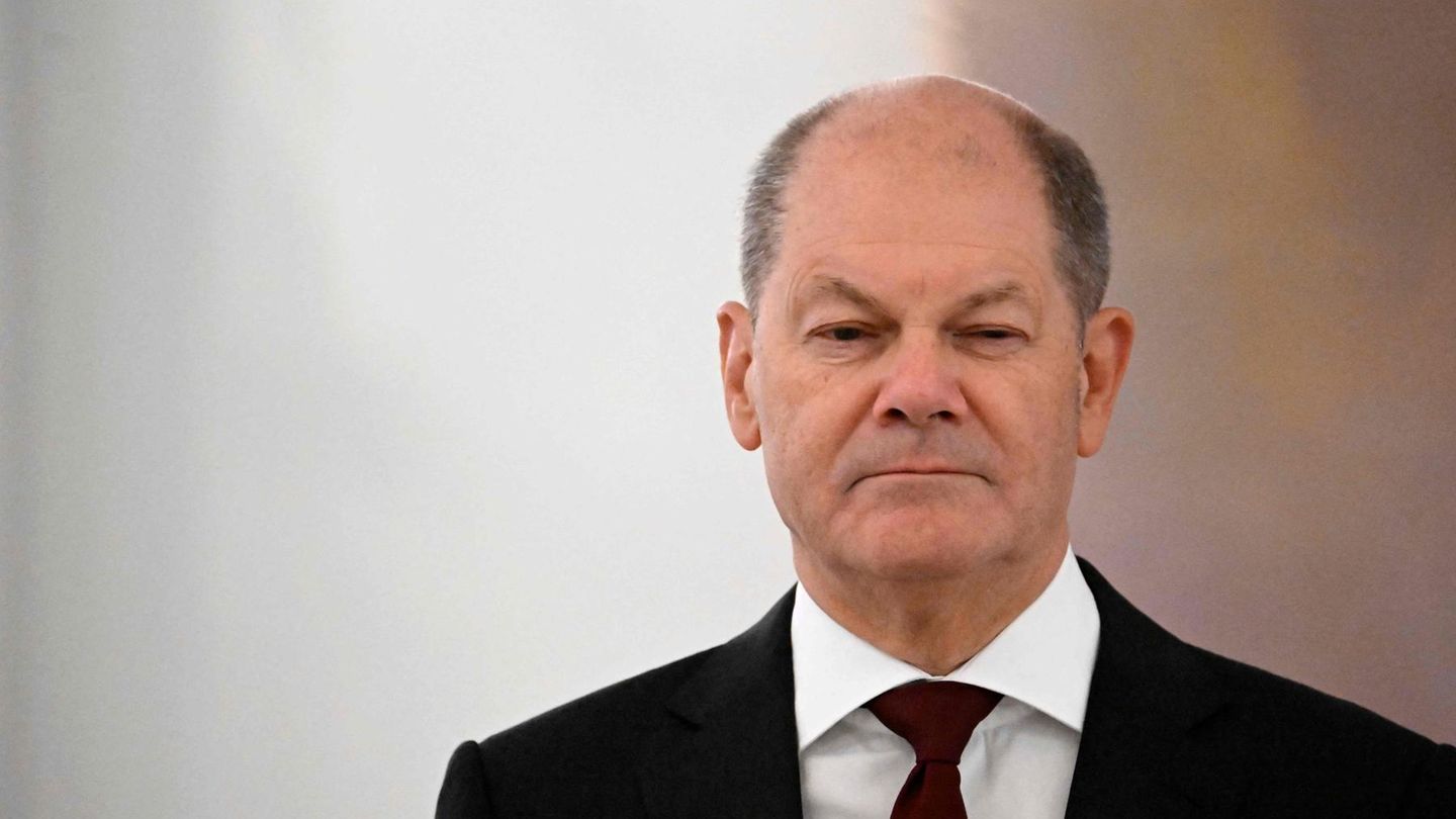 Olaf Scholz steht mit heruntergezogenen Mundwinkeln im schwarzen Anzug in einem Saal des Schlosses Bellevue