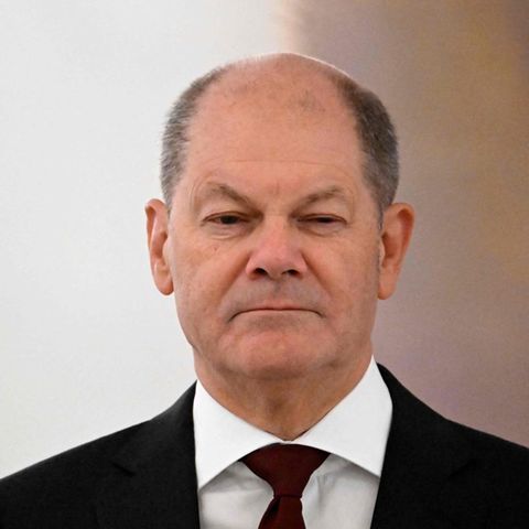 Olaf Scholz steht mit heruntergezogenen Mundwinkeln im schwarzen Anzug in einem Saal des Schlosses Bellevue