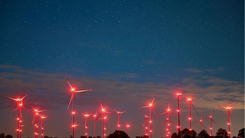 Rote Positionslichter an Windenergieanlagen erhellen den Nachthimmel und die Landschaft