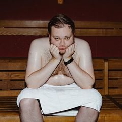 Ein Mann sitzt mit weißem Handtuch in der Sauna und schwitzt, den Kopf auf die Hände gestützt