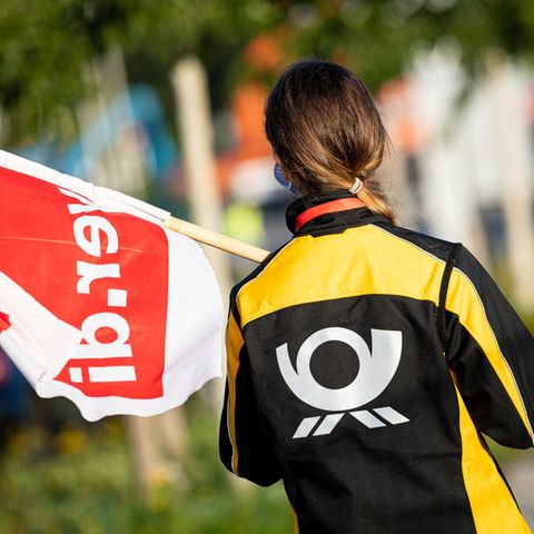 Eine Beschäftigte der Deutschen Post steht mit einer Fahne der Gewerkschaft Verdi vor einer Deutsche-Post-DHL-Niederlassung