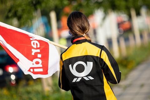 Eine Beschäftigte der Deutschen Post steht mit einer Fahne der Gewerkschaft Verdi vor einer Deutsche-Post-DHL-Niederlassung