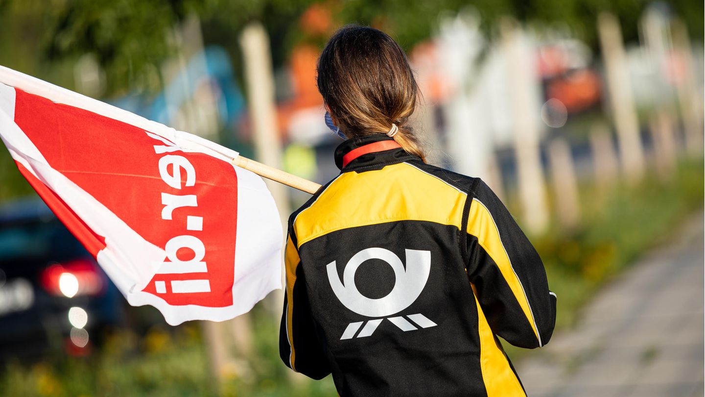 Eine Beschäftigte der Deutschen Post steht mit einer Fahne der Gewerkschaft Verdi vor einer Deutsche-Post-DHL-Niederlassung