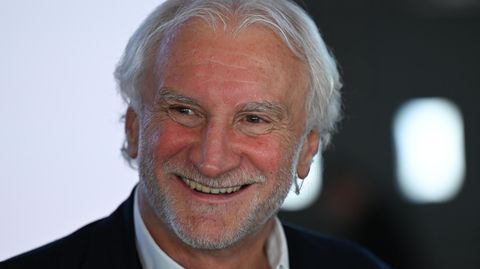 Rudi Völler lächelt breit und schaut dabei an der Kamera vorbei