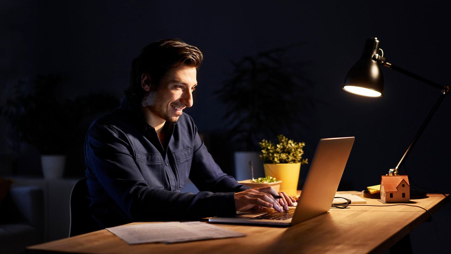 Ein Mann sitzt vor einem Laptop. Er arbeitet vermutlich Online.