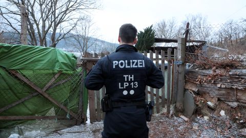 Mit dem Rücken zur Kamera steht ein Thüringer Polizist am Gartenzaun eines Grundstücks in Bad Blankenburg