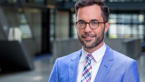 Michael Stempfle, ein weißer Mann mit braunem Seitenscheitel und Drei-Tage-Bart, trägt Hornbrille und einen hellblauen Anzug