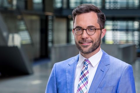 Michael Stempfle, ein weißer Mann mit braunem Seitenscheitel und Drei-Tage-Bart, trägt Hornbrille und einen hellblauen Anzug