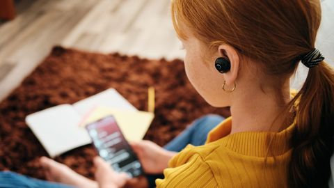 Deals und Angebote: Rothaariges Mädchen sitzt mit Kopfhörern an ihrem Smartphone