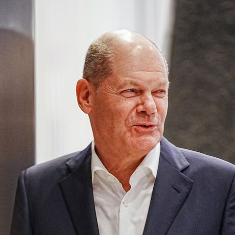 Olaf Scholz, ein älterer weißer Mann mit Halbglatze geht im Anzug durch eine Tür