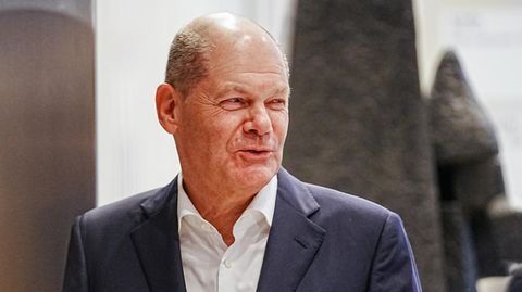 Olaf Scholz, ein älterer weißer Mann mit Halbglatze geht im Anzug durch eine Tür
