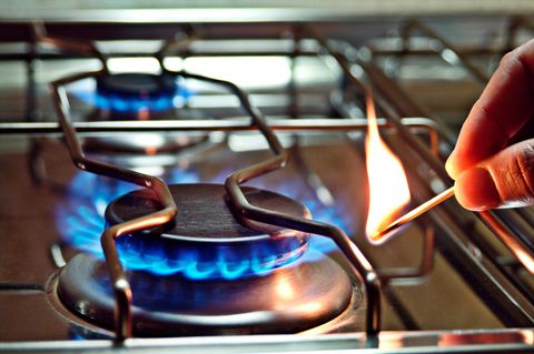 Die Flamme eines Gasherdes wird mit einem Streichholz angezündet