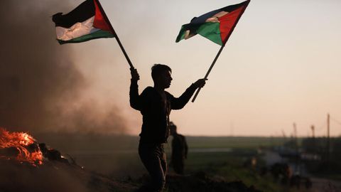 Ein Demonstrant hält palästinensische Fahnen neben brennenden Reifen