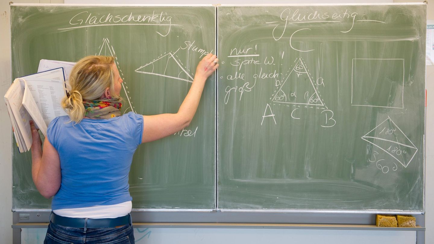 Eine Lehrerin schreibt mit Kreide an die Tafel