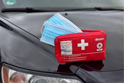 Ein Verbandskasten, aus dem zwei Schutzmasken herausragen, liegt auf einem Auto.