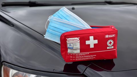 Ein Verbandskasten, aus dem zwei Schutzmasken herausragen, liegt auf einem Auto.