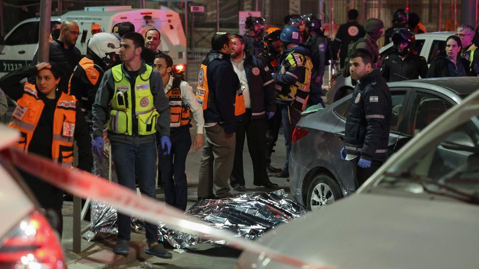 Vor einer Synagoge in Jerusalem liegt unter silberner Folie ein Leichnam. Rettungskräfte laufen in neonfarbenen Westen herum
