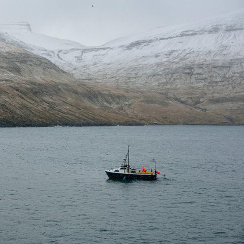Ein Fischerboot vor verschneiten Bergen der Färöer-Inseln