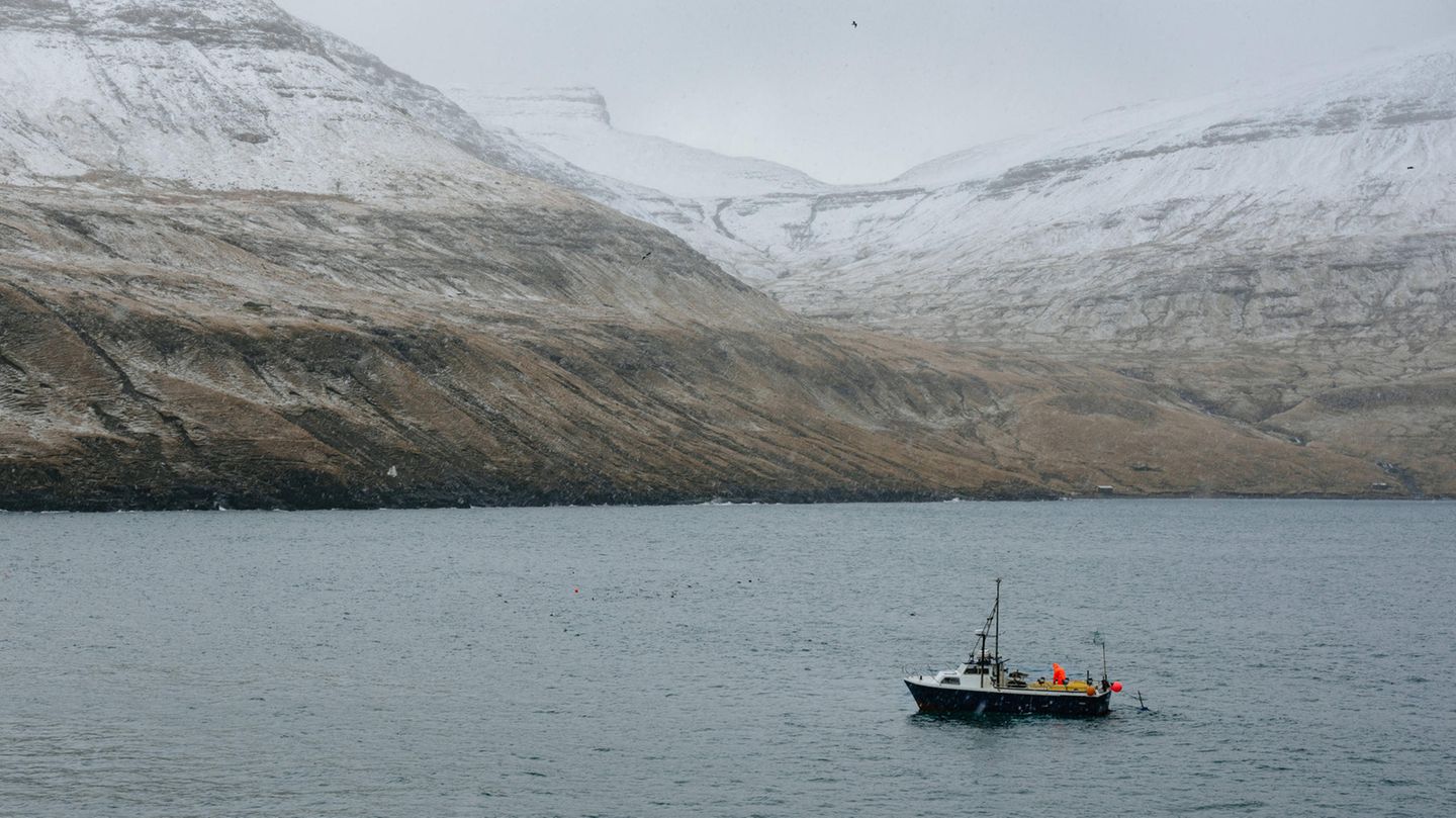 Ein Fischerboot vor verschneiten Bergen der Färöer-Inseln