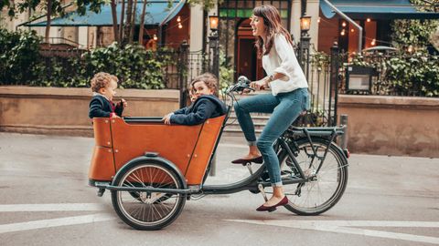 Eine Frau fährt mit drei Kindern in einem Lastenrad durch die Stadt