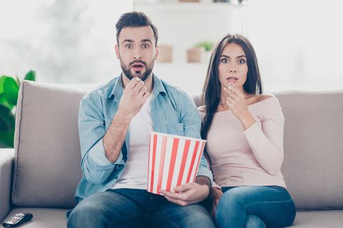 Paar schaut geschockt Richtung Fernseher