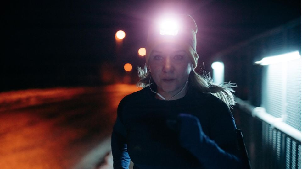 Eine Frau joggt mit Stirnlampe eine Straße entlang.