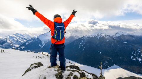 Backpacks für Wintersportler: Mann mit Skirucksack steht auf einem Gipfel mit Blick auf verschneite Berge